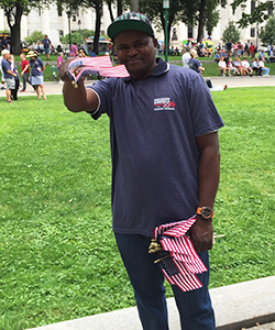 Colin Mbango pointing two American flags at camera