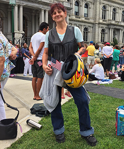 Karen Wagar standing with flag in one hand, motorcycle helmet in other