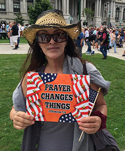 Lisa Sweeney in cowboy hat and sunglasses, holding "Prayer Changes Things" sign