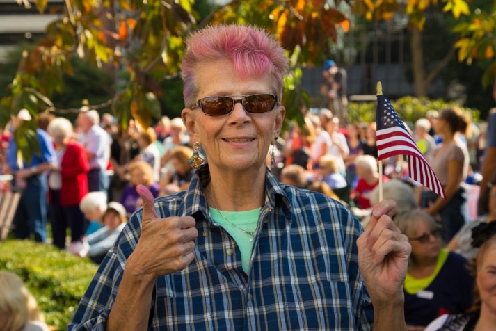 Woman with pink hair holding flag and giving a thumbs up