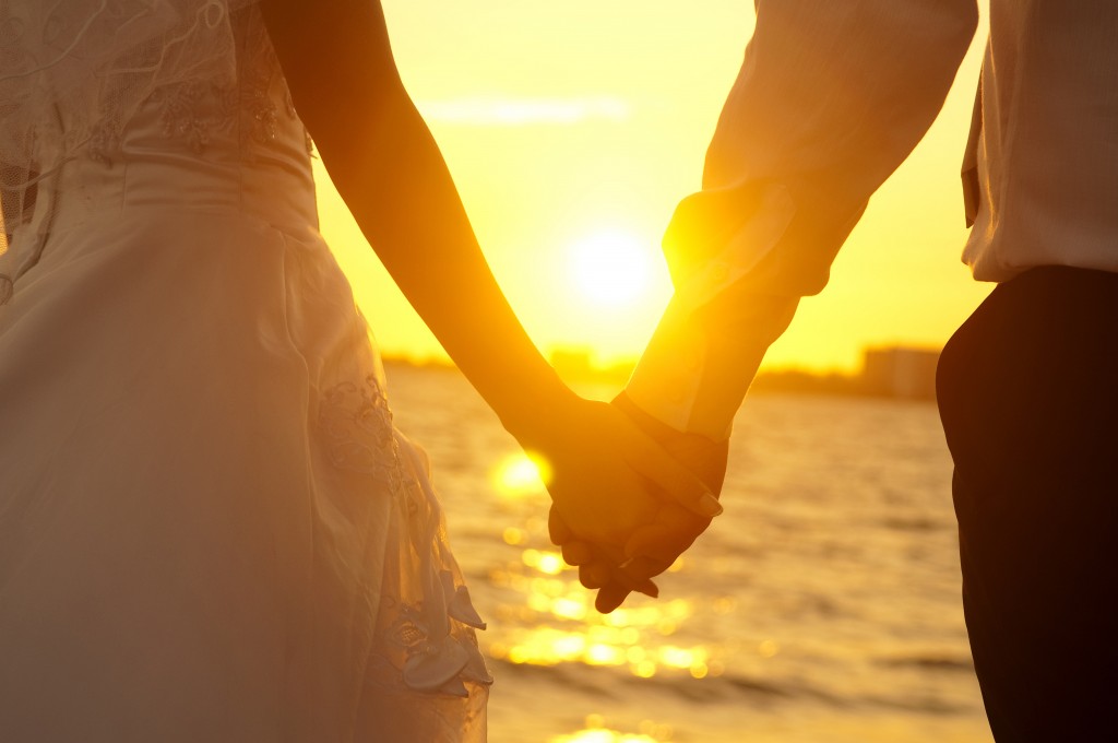 Bride and groom holding hands in front of sunset
