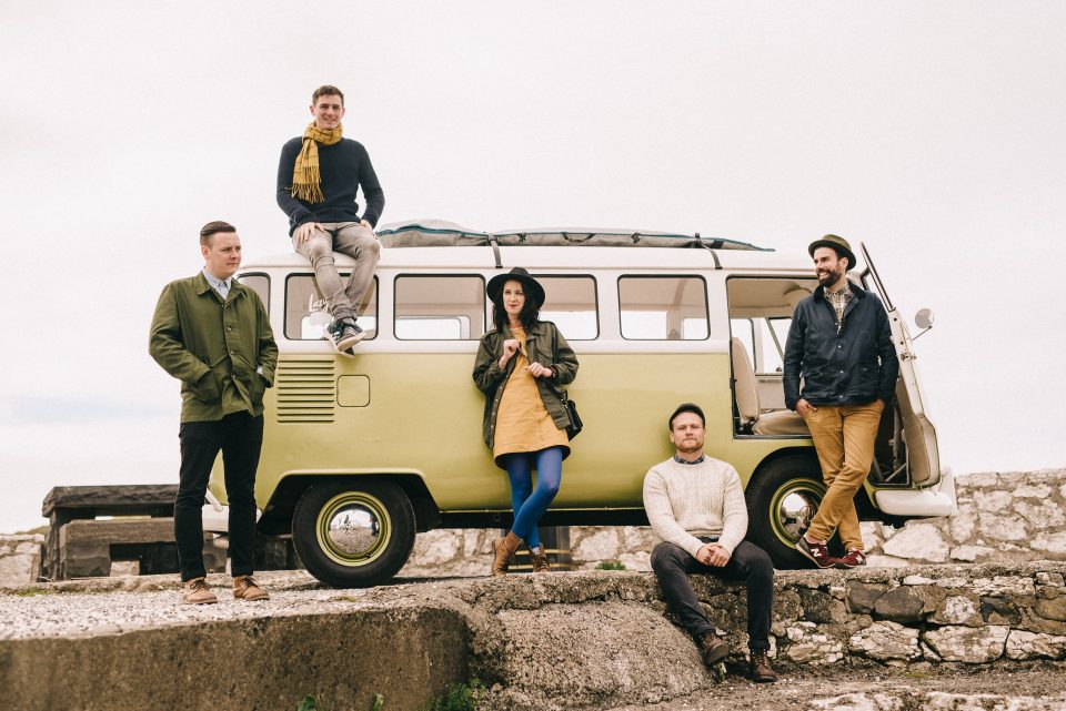 Band members sitting and standing around a van