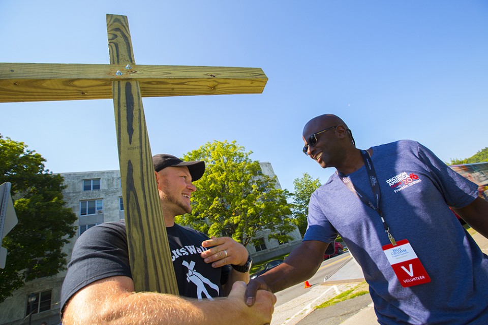 Man holding tall wooden cross, smiling and shaking hands with volunteer