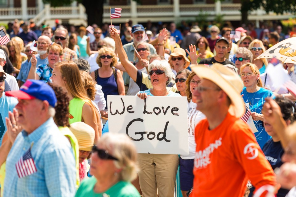 Woman holding "We love God" sign in crowd