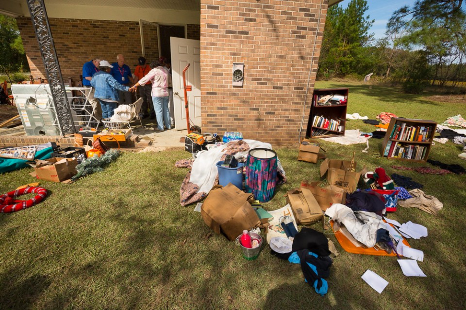 Household items, furniture, clothing on grass outside flooded house