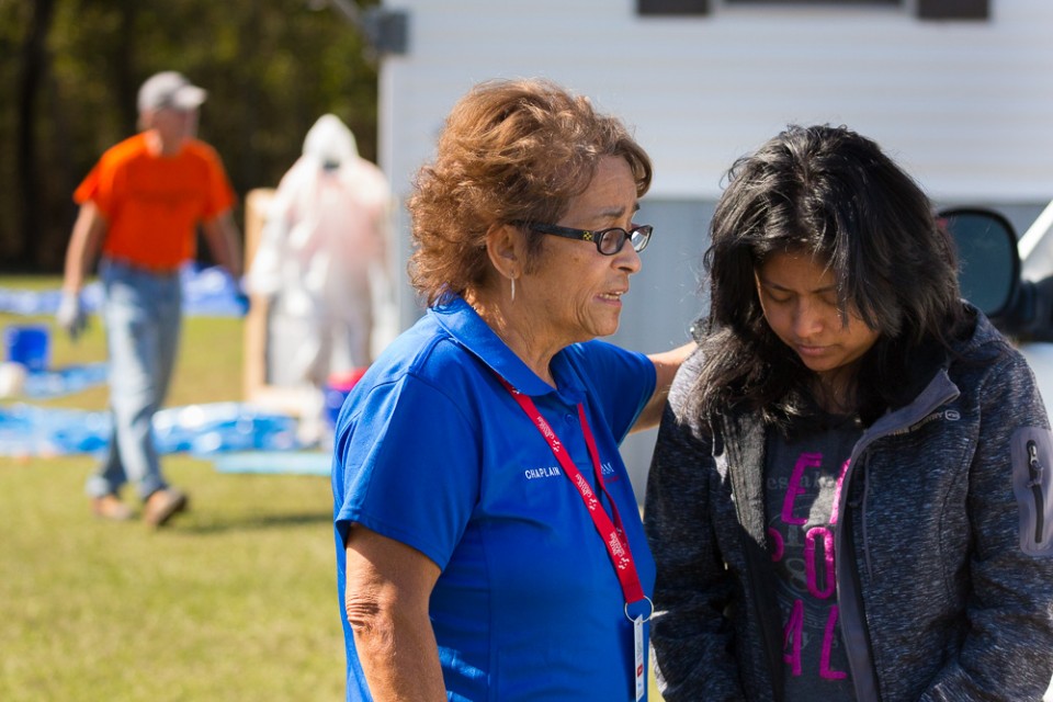 Billy Graham RRT Chaplain praying with woman (flood victim); men cleaning out underneath mobile home