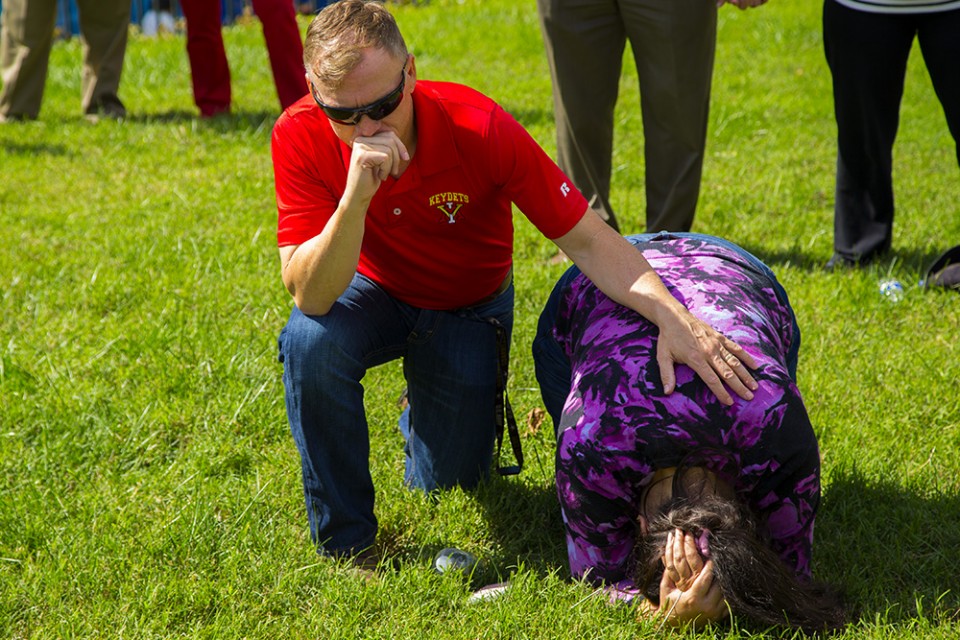 Man kneeling in prayer and woman with head down on grass in prayer