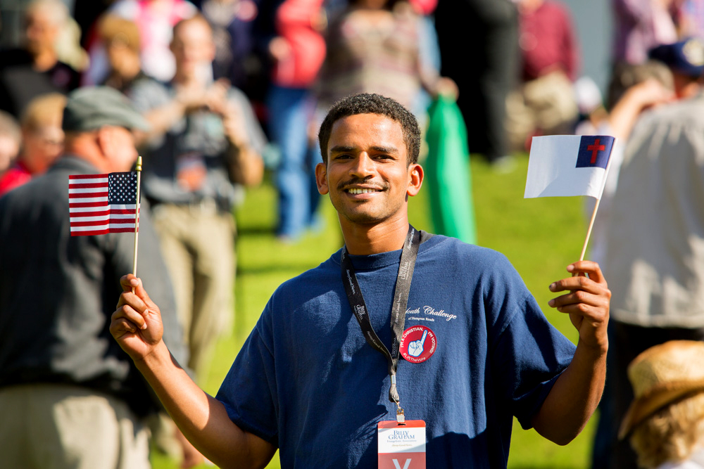 Young man, a volunteer, smiling and holding American flag and Christian flage