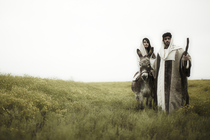 Joseph leading Mary on a donkey in field