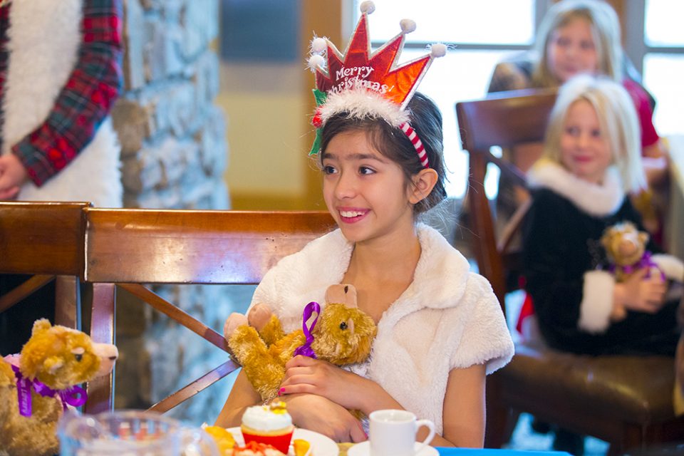 Girl smiling and holding stuffed camel; wearing 'Merry Christmas' headband