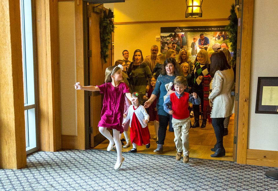 Girl skipping down the hall; other children parents behind her