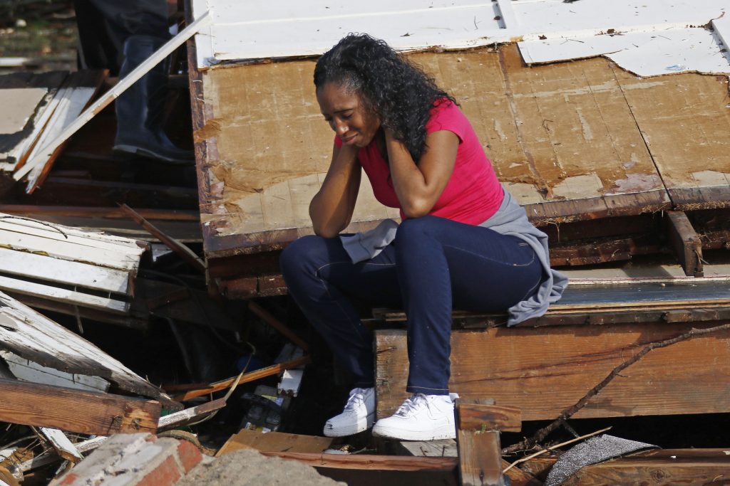 Woman sitting on debris with hands to face, crying