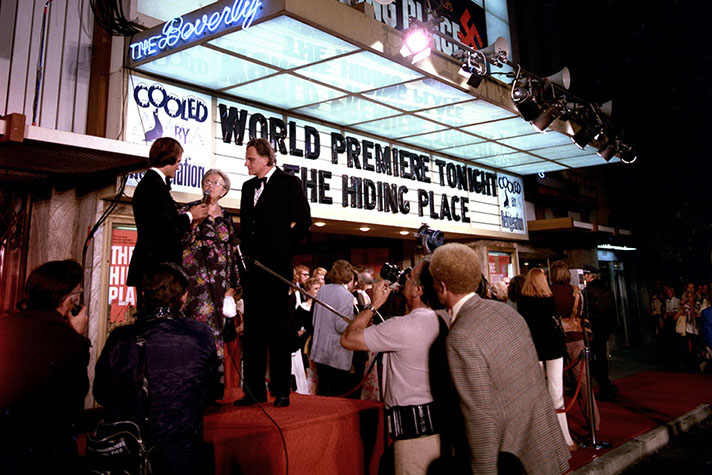 Billy Graham stands with Corrie ten Boom and entertainer Pat Boone in front of a marquee that advertises The Hiding Place world premiere