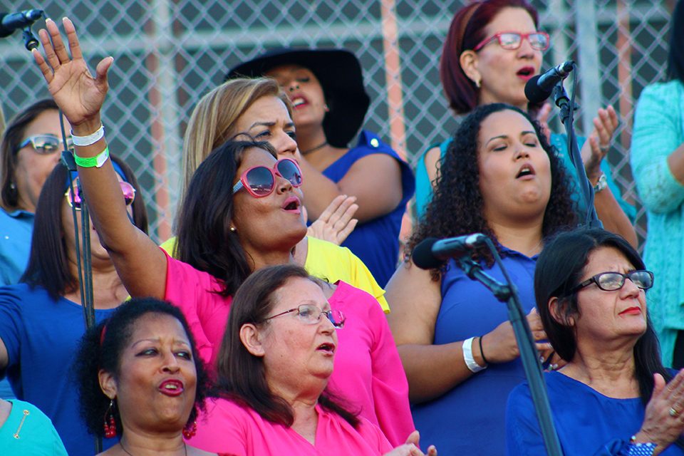 woman in pink shirt and sunglasses singing, arm outstretched