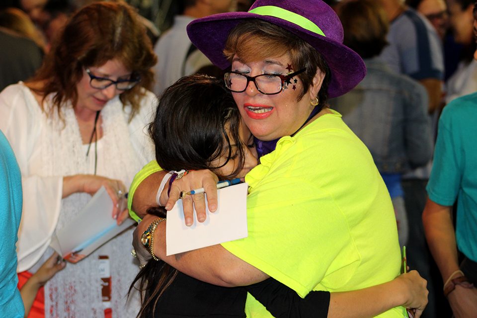 Woman in yellow shirt and purple hat hugging young girl