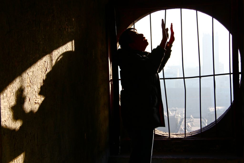 Man standing in jail cell with arms lifted in worship