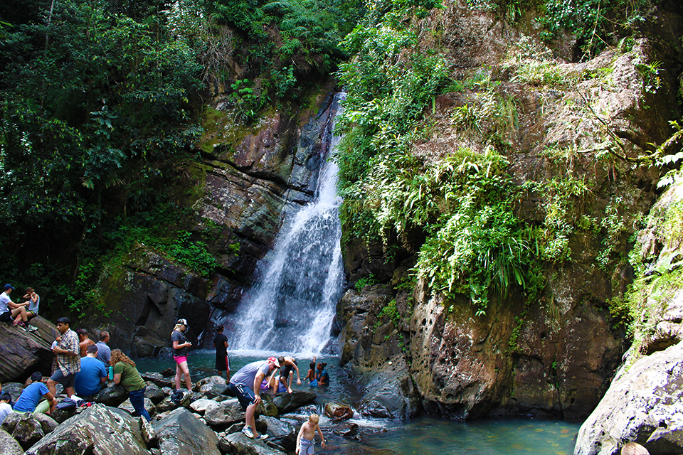 People sitting on rocks near waterfall in rain forest