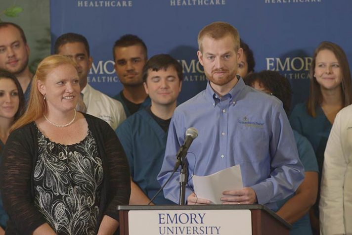 Kent Brantly and wife, Amber, stand at podium, doctors and nurses behind them