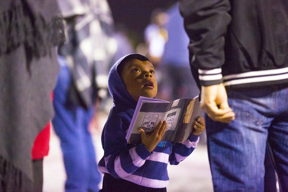 Little boy holding Celebration materials and looking up to adult