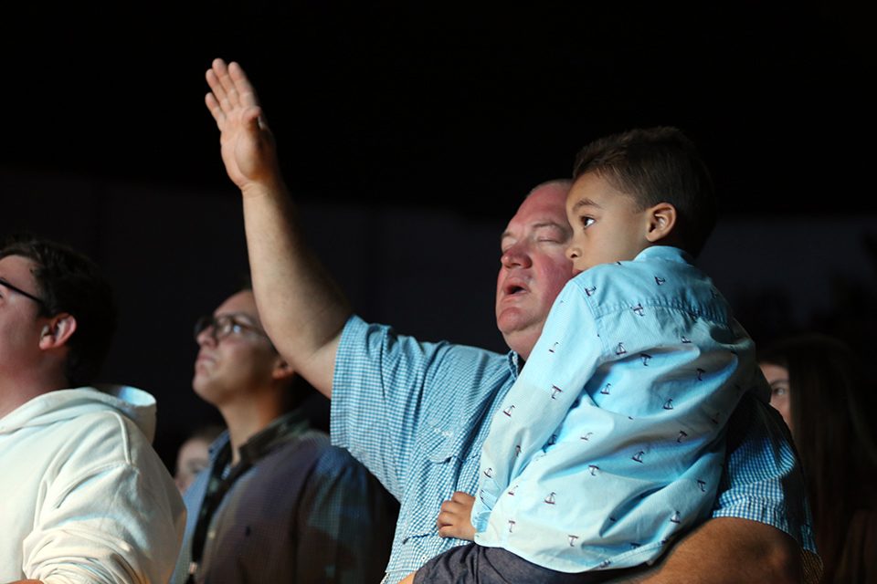 Man with arm raised in worship, holding little boy