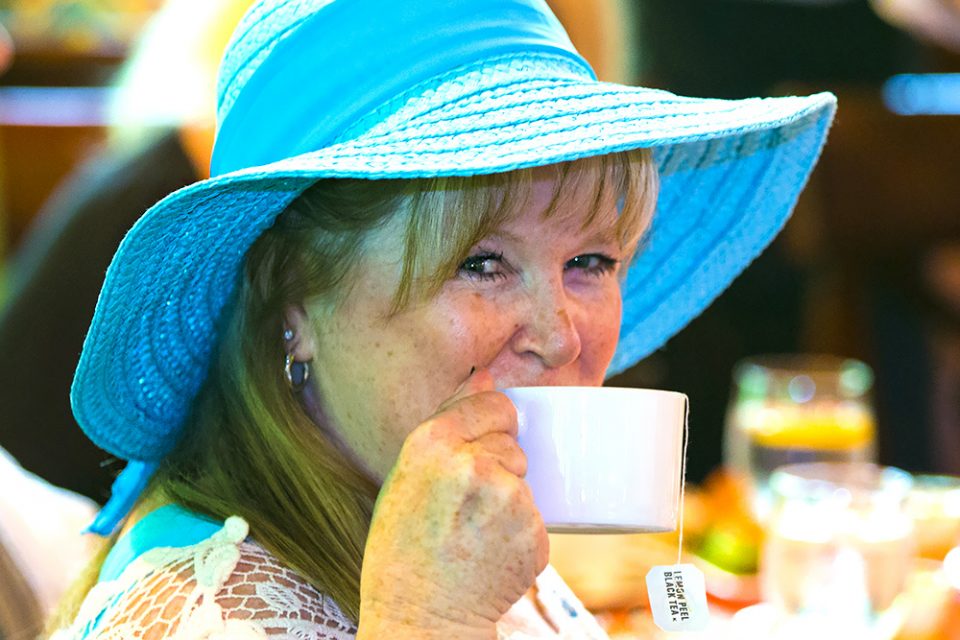 woman wearing blue floppy hat sipping on tea
