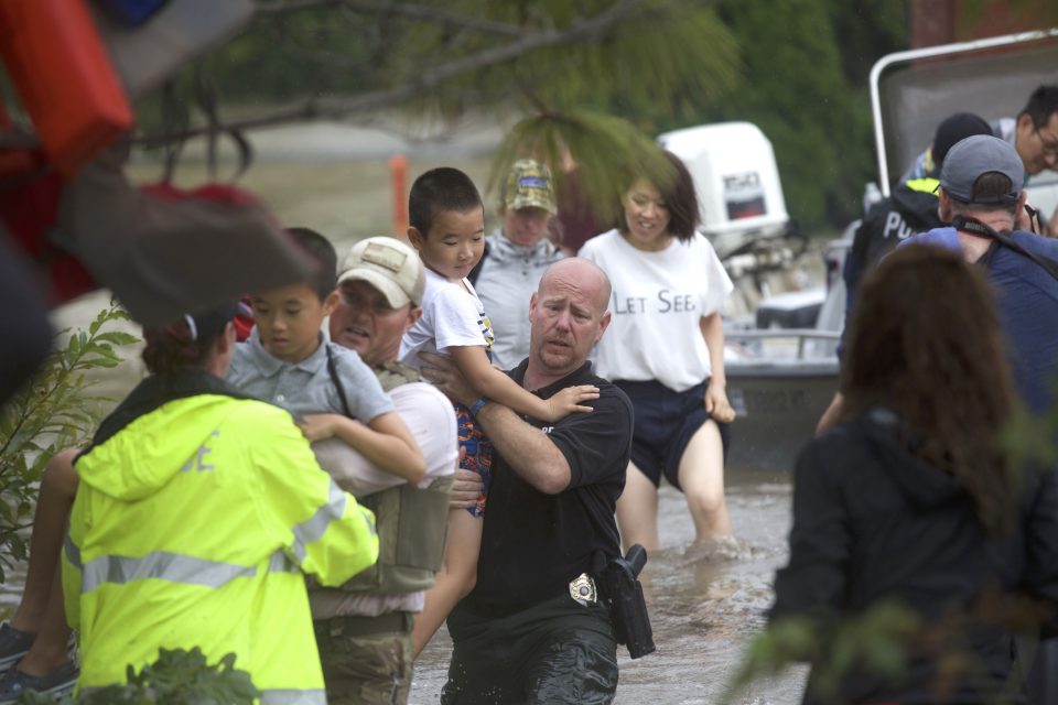 Emergency personnel carry young boys from boat through floodwaters