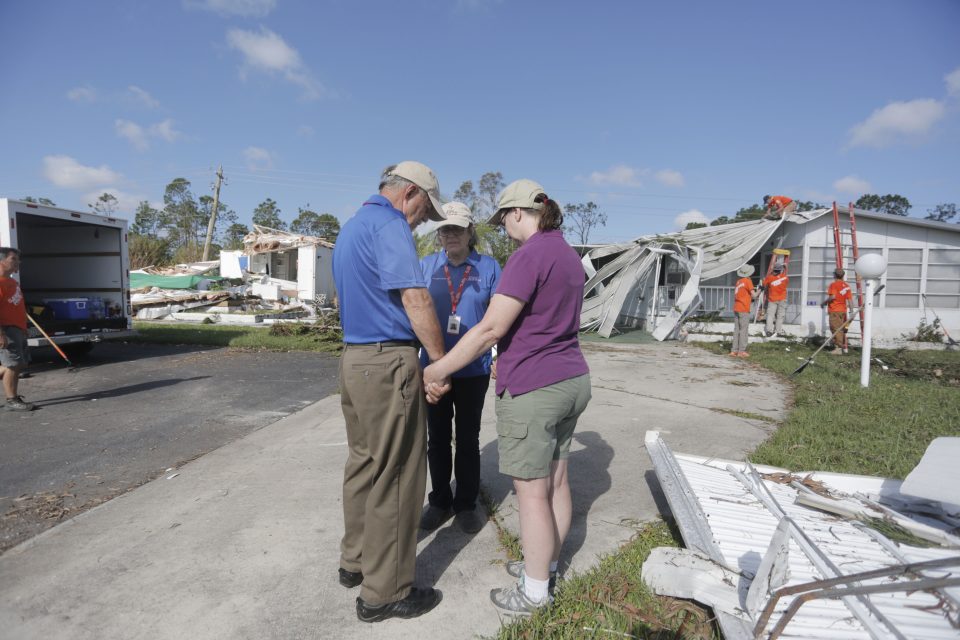 Chaplains pray with a Naples resident. In the background are heavily damage homes