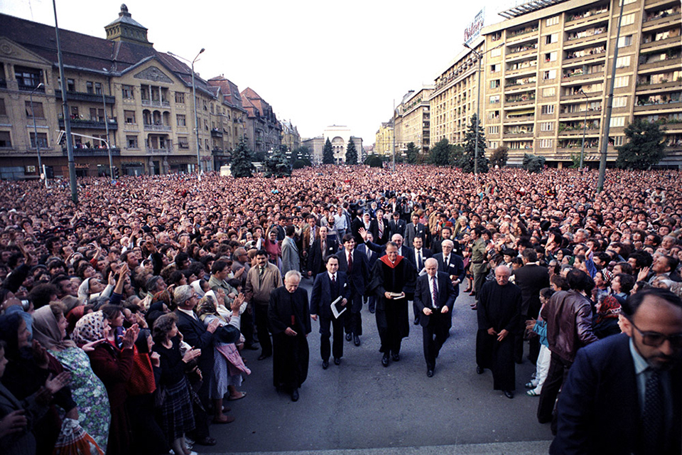 Billy Graham walking through street in Romania, large crowd gathered around