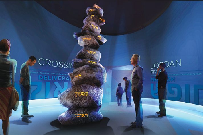 Visitors looking at a tall structure of stones with illuminated writing on the side