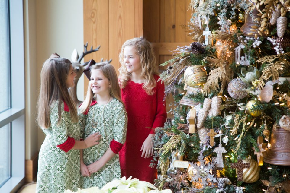 Three girls smile around the Christmas tree