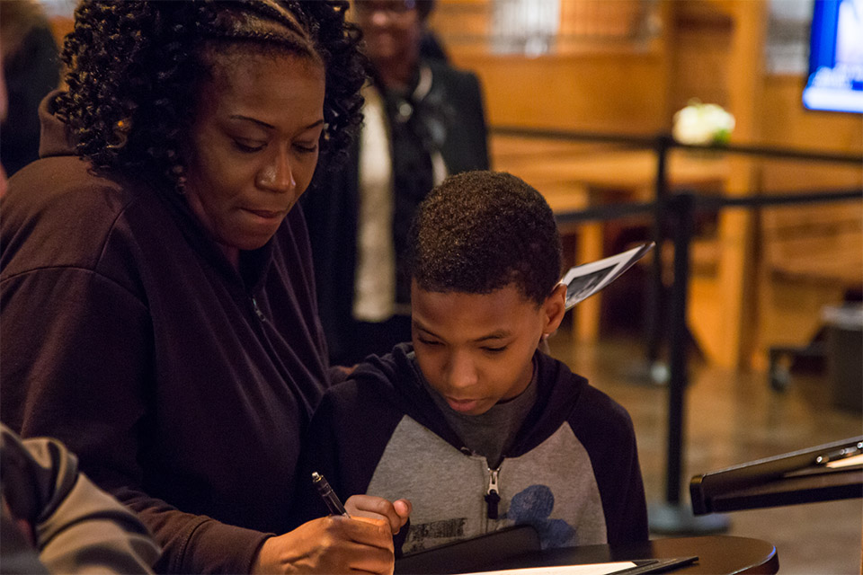 Son watching his mother sign the guest register.