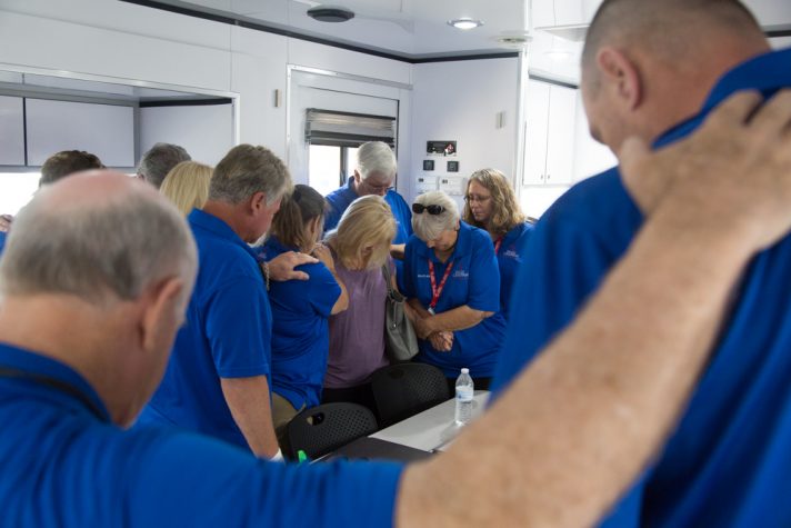 Chaplains in blue shirts huddled around woman in prayer