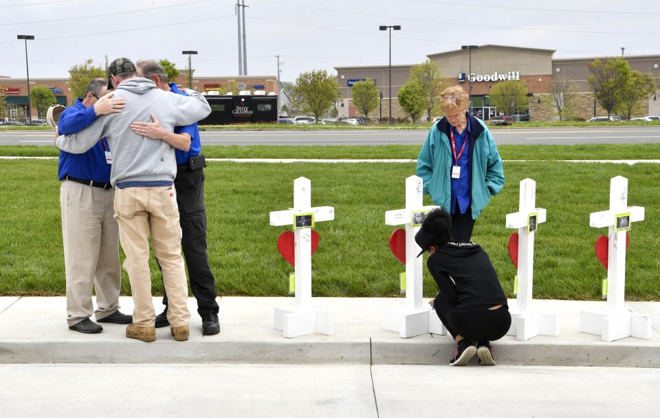 Chaplains in prayer with people in front of four white crosses; woman kneeling down before a cross