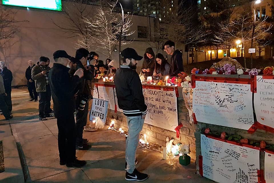 People gathered around memorial site; lit candles all around