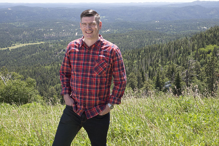 Will Graham standing atop a green mountain with trees below