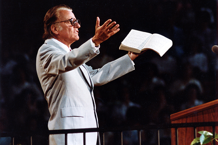 Billy Graham with Bible in hand, arms open, preaching