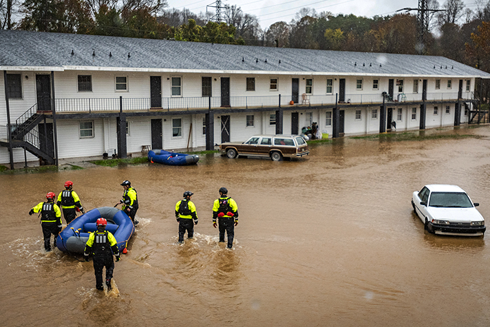 Rescuers in knee-deep water with raft outside apartments