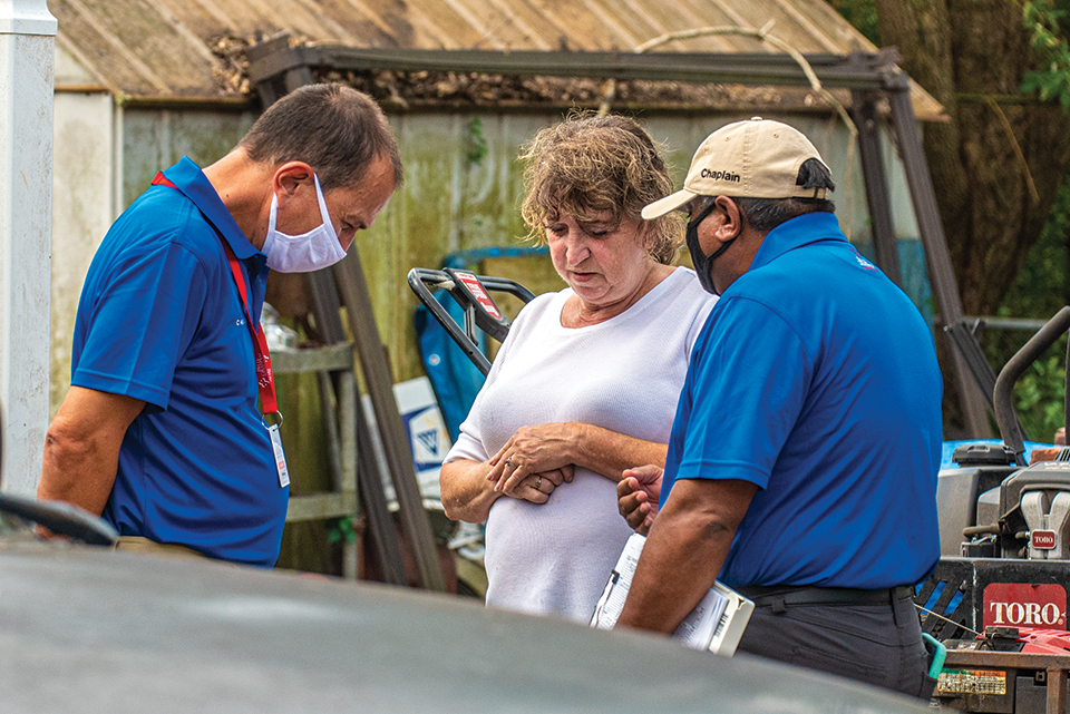 Two male chaplains bowing heads to pray with woman