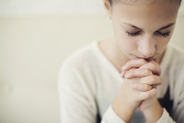 Young girl with head bowed and hands folded, praying