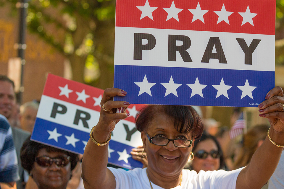 Woman holding up red, white and blue sign that says "pray."