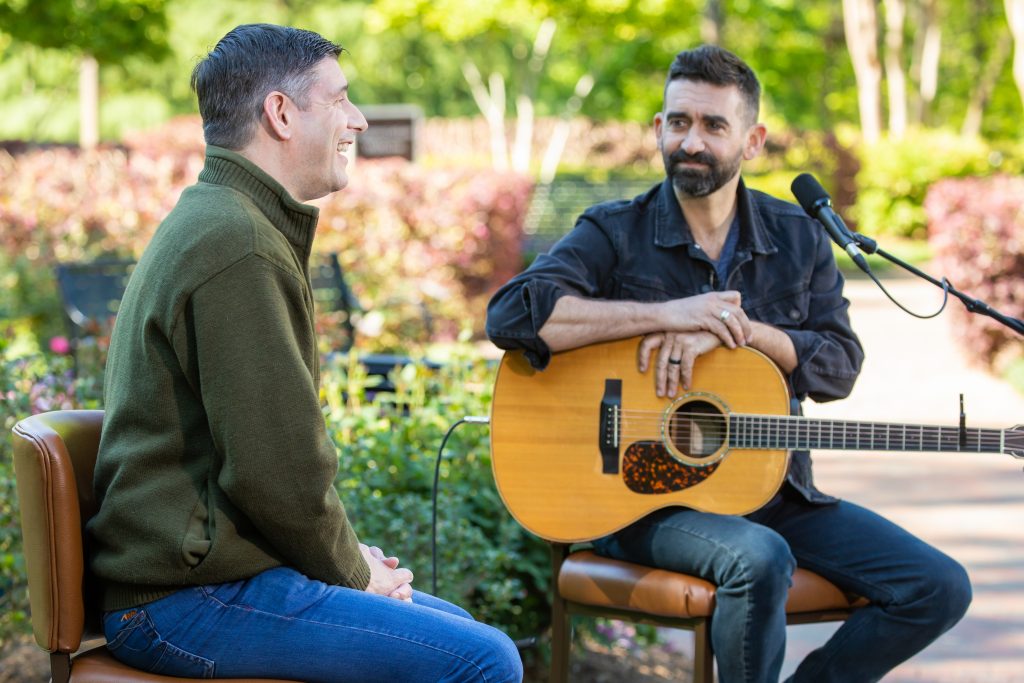 Will Graham and Aaron Shust sit on chairs outside, Aaron Shust with a guitar in his lap