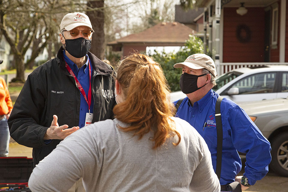 Two chaplains in baseball hats speak with woman