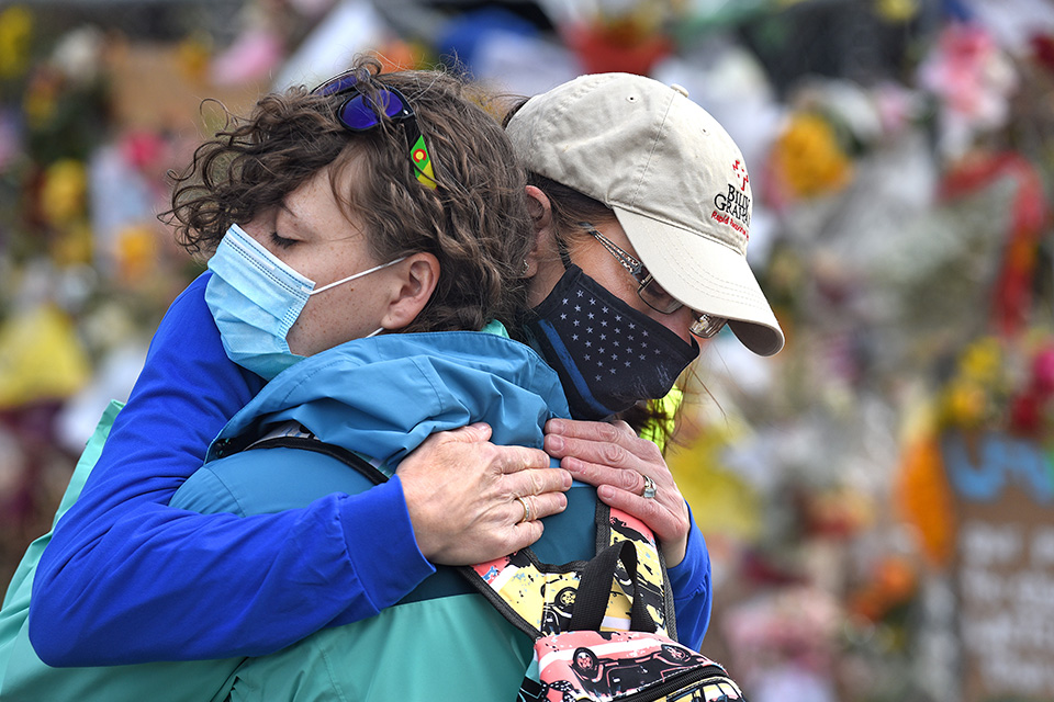 Chaplain hugs woman in front of memorial, both women in masks