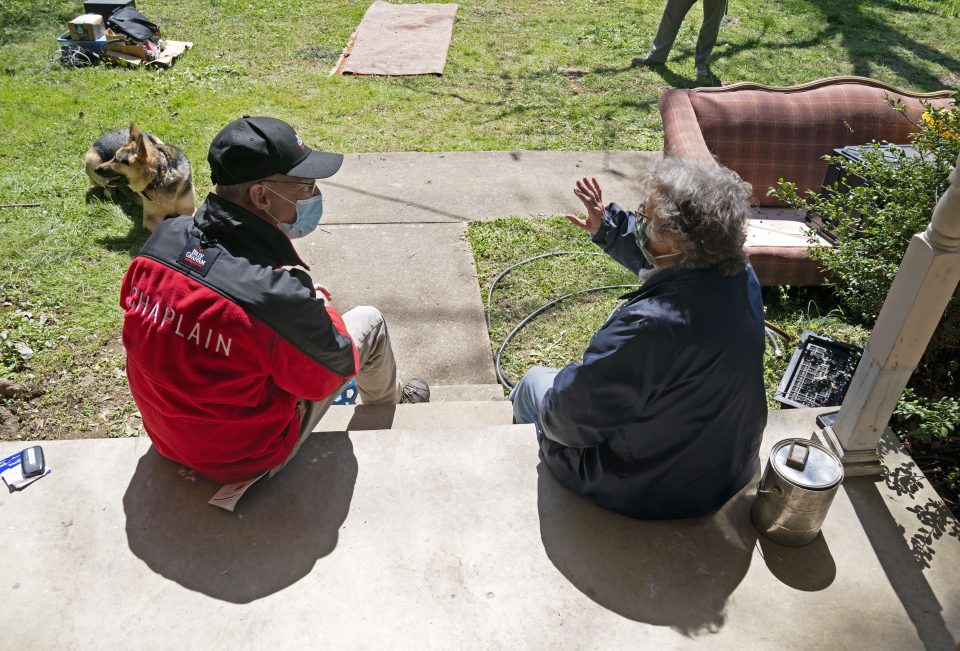 A chaplain sits with a woman on her doorstep with her wet furniture in the lawn outside