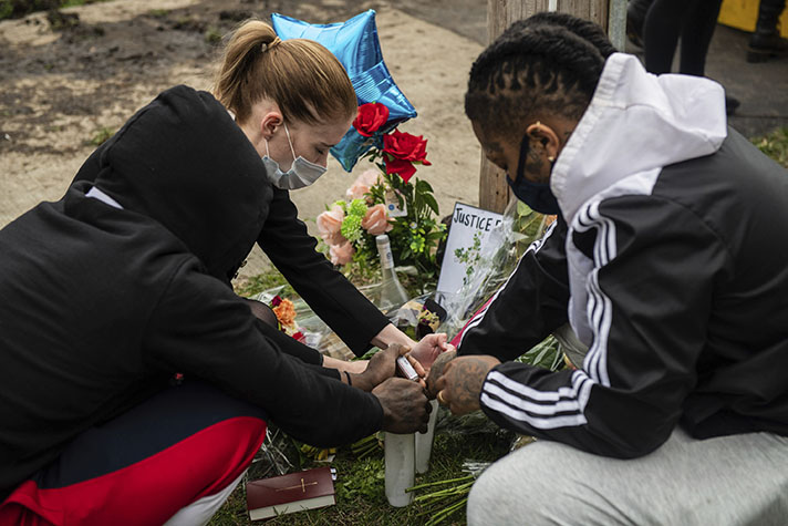 Three people kneeling down to light a candle on the ground