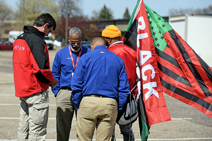 Chaplains gather in prayer with man holding Black Lives Matter flags