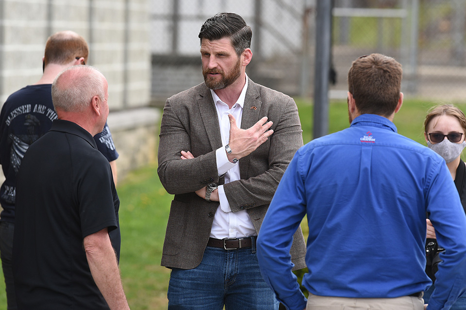 Edward Graham stands in suit coat, talking to officer and chaplain