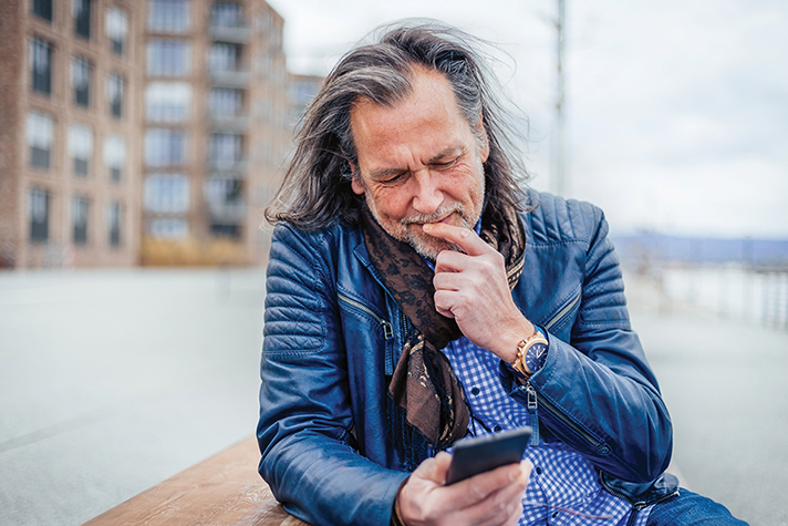 gray-haired man looks curiously at cellphone in hand