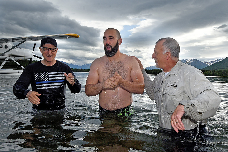 Three men stand waist-deep in water, seaplane floating in background