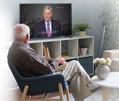 Older man sitting in chair seeing Franklin Graham on TV.
